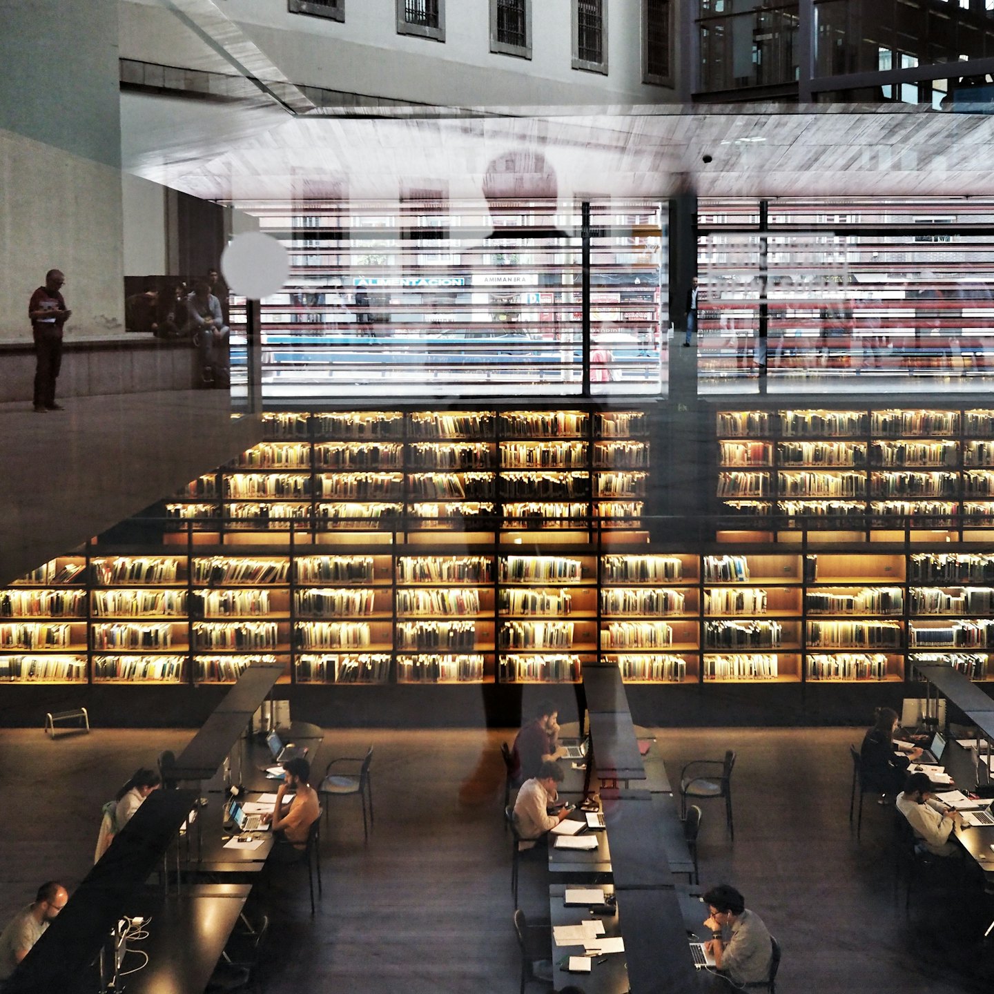 Gente estudiando y trabajando en una biblioteca moderna con muchas estanterías.